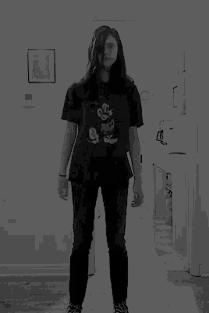 a woman wearing a mickey mouse t-shirt is dancing in a hallway