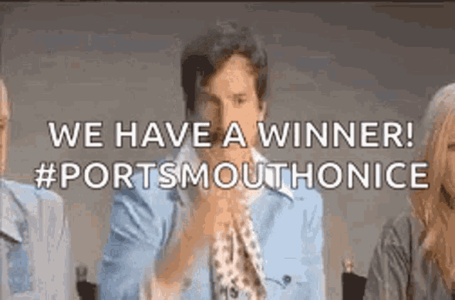 a man in a blue shirt and tie is sitting in front of a group of people and says `` we have a winner ! ''