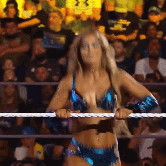 a woman in a bikini is standing in a wrestling ring with a crowd behind her