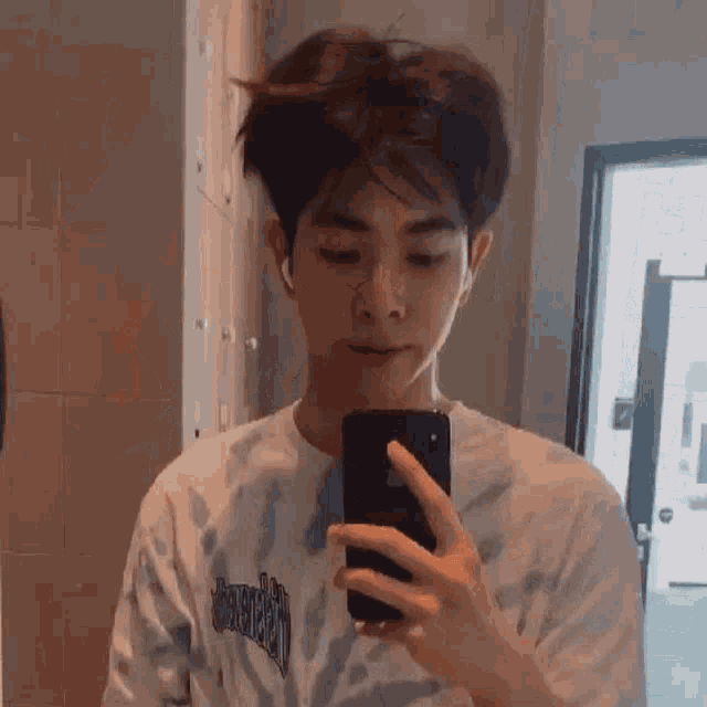 a young man is taking a selfie in front of a mirror with his phone .