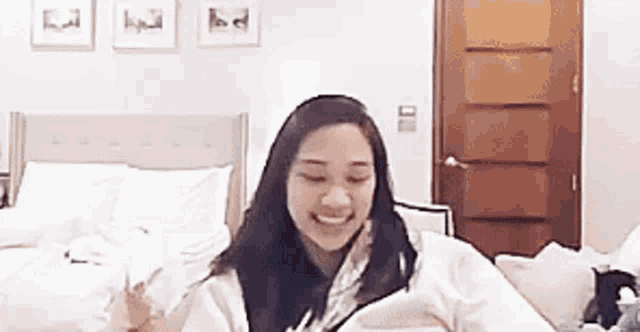 a woman is sitting on a bed with a blanket on her head and smiling .
