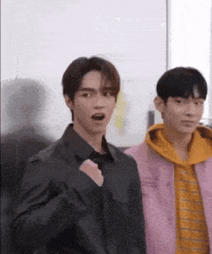 two young men are standing next to each other in a room . one of the men is wearing a pink jacket .