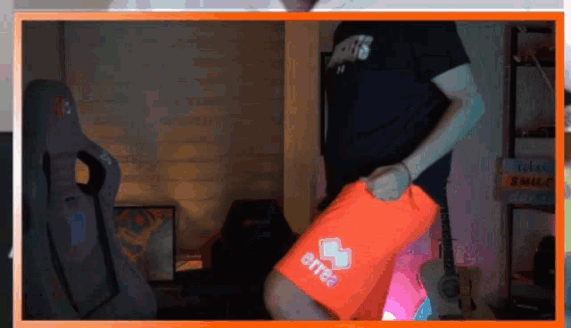 a man in a black shirt is holding an orange shorts that say errea