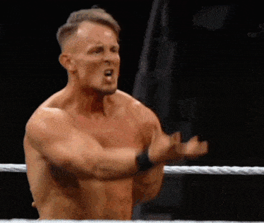 a man without a shirt is standing in a wrestling ring with his hands outstretched .
