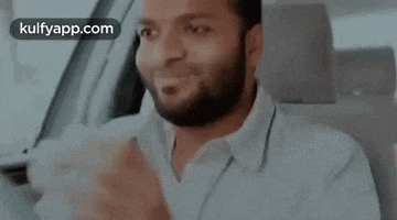 a man with a beard is sitting in the driver 's seat of a car and making a funny face .