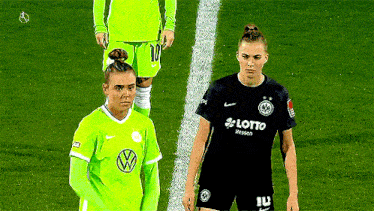 two female soccer players are standing on a field .