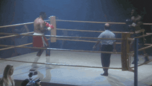 a man is laying on the ground in a boxing ring while another man watches