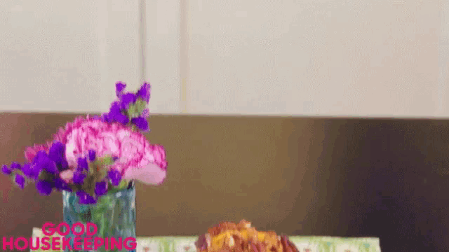 a vase of pink and purple flowers sits on a table with the words good housekeeping written on it