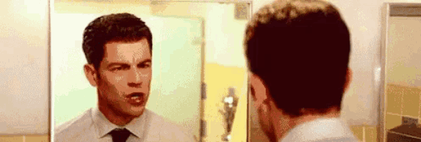 a man in a white shirt and tie is looking at himself in a bathroom mirror .