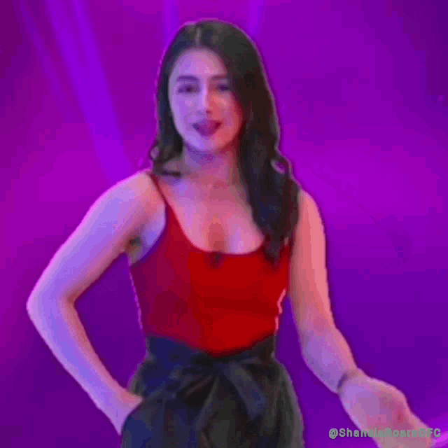 a woman in a red tank top is standing in front of a purple background .