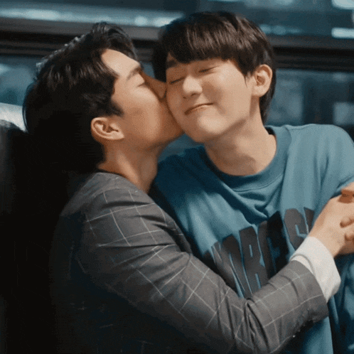 a man kissing another man on the cheek who is wearing a blue shirt that says ' a ' on it