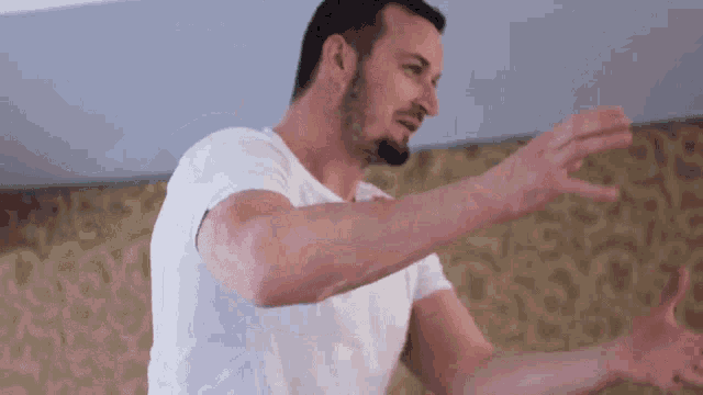 a man in a white shirt is standing with his arms outstretched in front of a gold wall .
