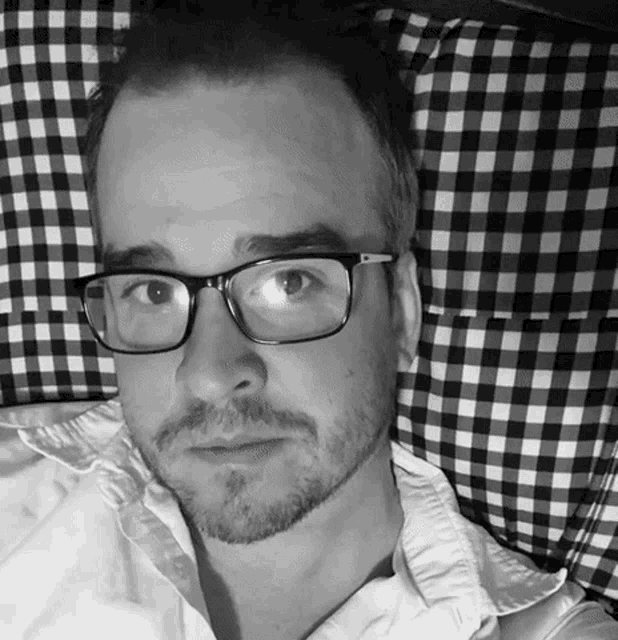a man wearing glasses is laying on a bed