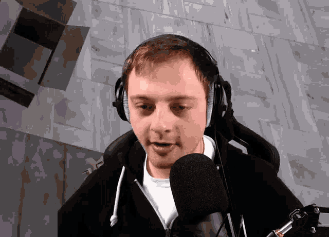 a man wearing headphones and a black hoodie is speaking into a microphone