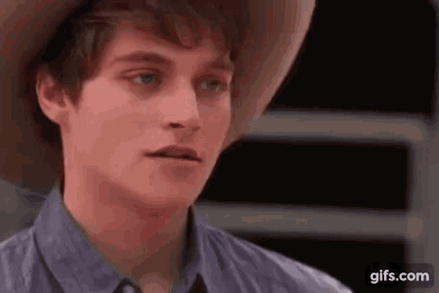 a close up of a young man wearing a cowboy hat and a blue shirt .