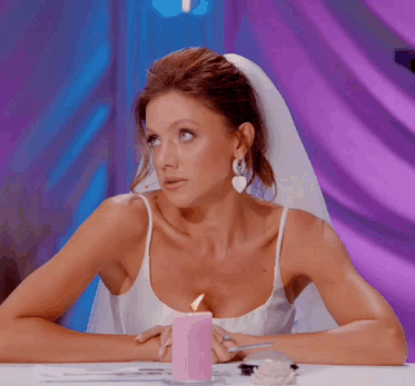 a woman in a wedding dress is sitting at a table with a pink candle in front of her