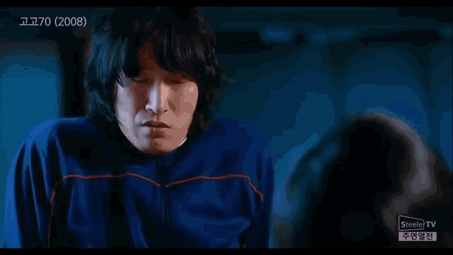 a man in a blue sweater is looking at another man in a dark room .