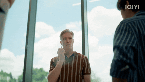 a man in a striped shirt talks on a cell phone in front of a window
