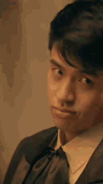 a young man in a tuxedo and tie is looking at the camera .