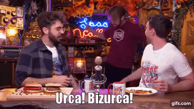a group of men are sitting at a table with food and a sign that says urca bizurca ..