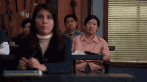 a group of people are sitting in a classroom with a woman sitting at a desk .