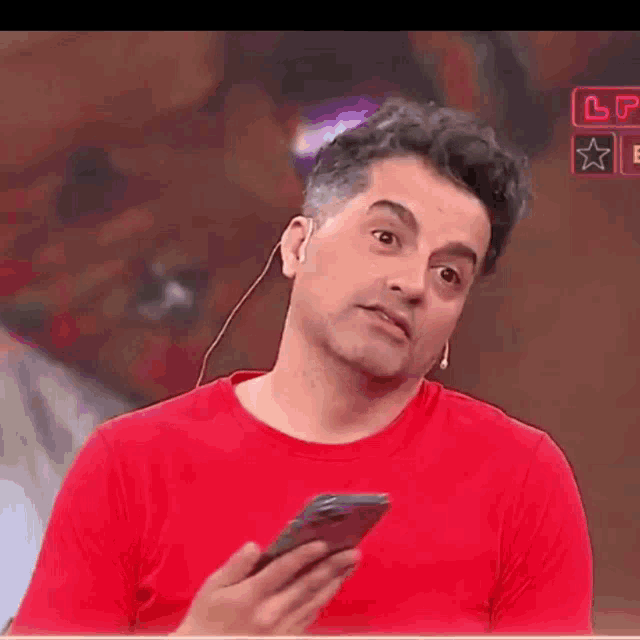 a man in a red shirt is holding a cell phone