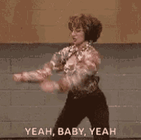 a man wearing headphones is dancing in front of a brick wall and saying yeah , baby , yeah .