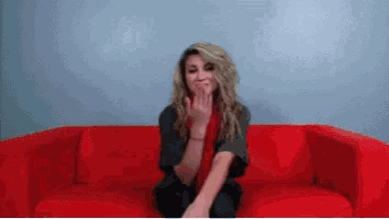 a woman sitting on a red couch covering her mouth with her hands