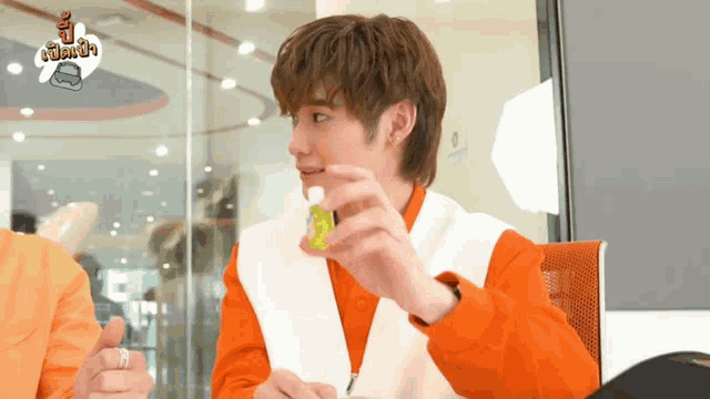 a young man in an orange jacket is holding a small bottle of liquid in his hand .