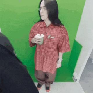 a woman in a red plaid shirt is standing in front of a green wall holding a cup of coffee .