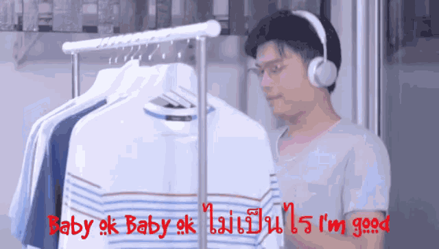 a man wearing headphones stands in front of a rack of clothes with the words baby ok baby ok i 'm good