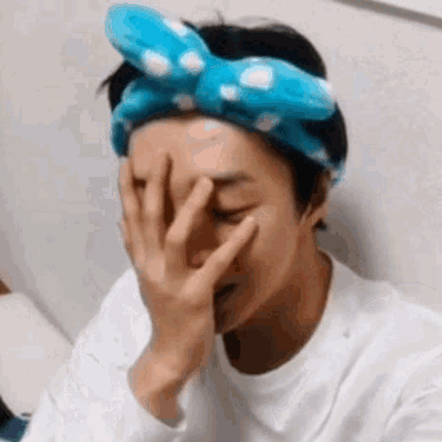 a man wearing a headband is covering his face with his hand .