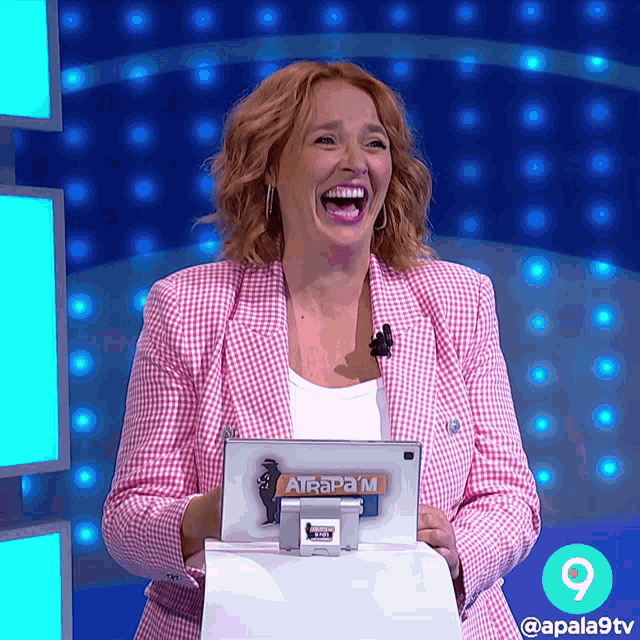 a woman in a pink jacket is laughing while holding a tablet that says atrapam on it