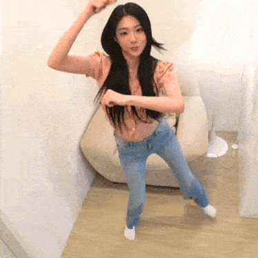 a woman in a pink shirt and blue jeans is dancing in a room