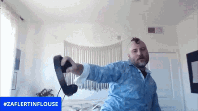 a man in a blue shirt is holding a telephone in front of a screen that says #zaflertinflouse
