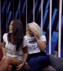 two women are sitting next to each other on a couch and one is laughing