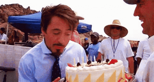a man is blowing out candles on a birthday cake while another man looks on .