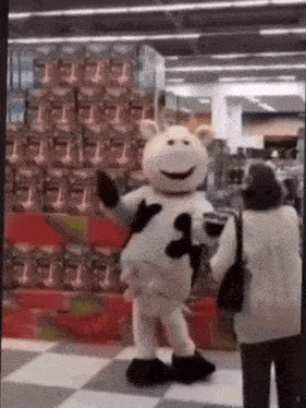 a mascot in a cow costume is dancing in a store .