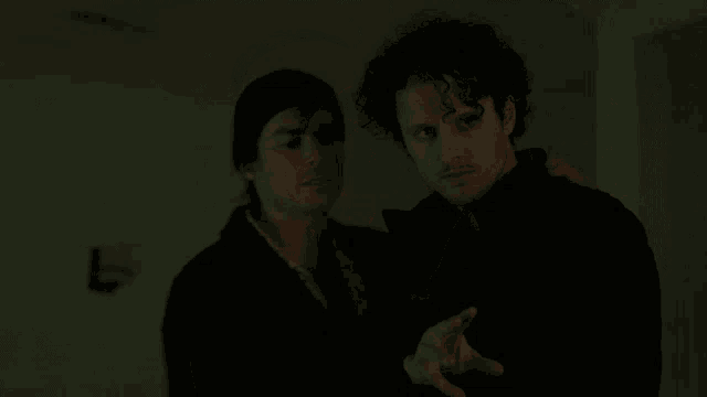 two men are standing next to each other in a dark room and holding hands .