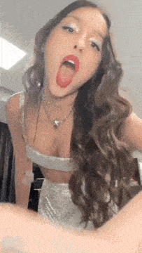 a woman with long hair is sticking her tongue out while wearing a silver top and skirt .