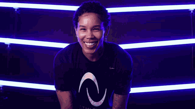 a woman in a black nike shirt smiles in front of purple lights