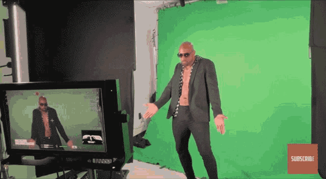 a man in a suit is standing in front of a green screen with a subscribe button