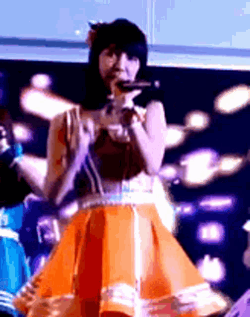 a woman in an orange dress is singing into a microphone on a stage