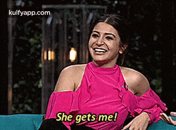 a woman in a pink top is sitting on a blue couch laughing and saying she gets me .