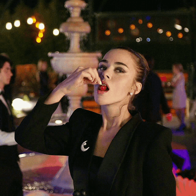 a woman in a black tuxedo is eating a red candy