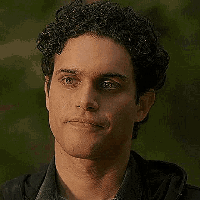 a close up of a man 's face with curly hair and a black jacket .
