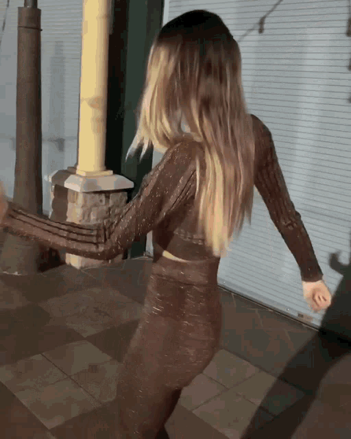 a woman in a brown top and pants is dancing on the sidewalk