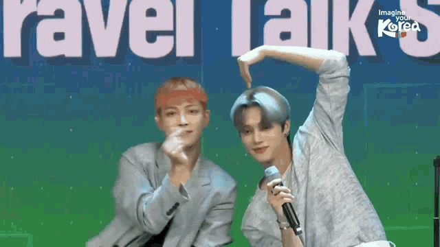 two men are making a heart shape with their hands while standing next to each other on a stage .