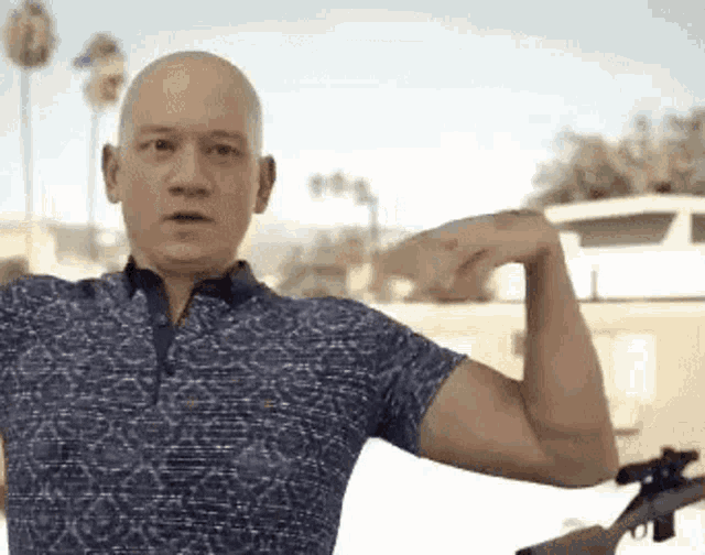 a bald man is flexing his muscles while holding a gun .
