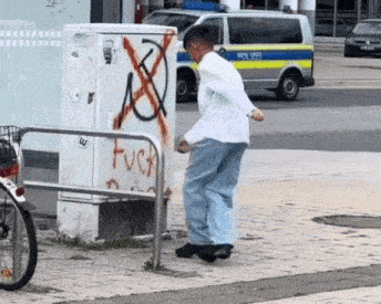 a man is standing on a sidewalk next to a graffiti covered box .
